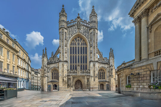 Frontalansicht der gotischen Abteikirche am leeren gepflasterten Vorplatz im historischen Stadtzentrum von Bath unter blauem Himmel.