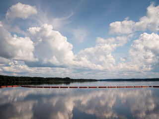 Serene lake mirrors fluffy white clouds overhead. Red buoys line horizon, calm water reflects sky. Peaceful scene ideal for travel, nature, or relaxation themes. Perfect for websites, magazines © mark_gusev