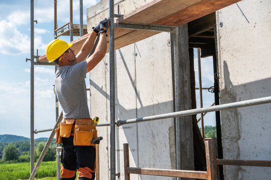 Construction worker assembling scaffolding beside a house
