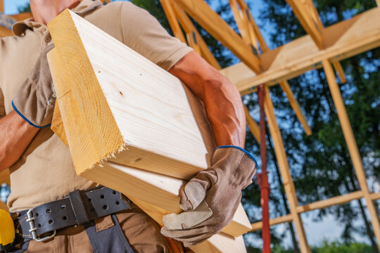 Carpenter carrying a timber beam at a roof construction site