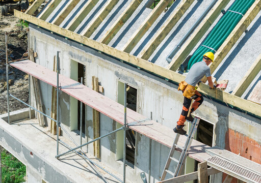 Worker on a ladder at the eaves of an unfinished house
