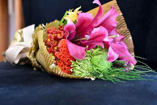 vibrant flower bouquet wrapped in textured kraft paper with burlap ribbon, floral arrangement with large pink lily and purple carnations against wooden background, gift bouquet close up