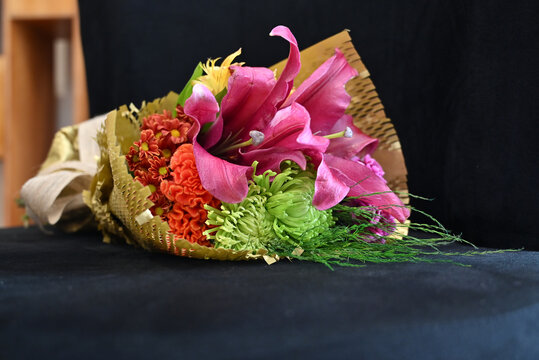 vibrant flower bouquet wrapped in textured kraft paper with burlap ribbon, floral arrangement with large pink lily and purple carnations against wooden background, gift bouquet close up