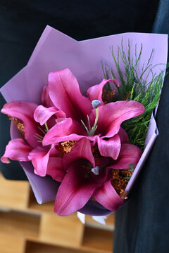 pink lily flower bouquet wrapped in light purple paper tied with satin ribbon, vibrant pink lilies floral arrangement resting on wooden table, elegant gift bouquet close up