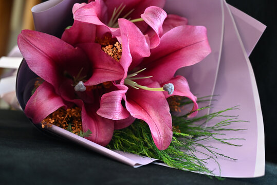 pink lily flower bouquet wrapped in light purple paper tied with satin ribbon, vibrant pink lilies floral arrangement resting on wooden table, elegant gift bouquet close up