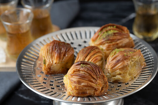 Turkish pastries, known as baklava, are arranged on a silver plate. In the background are glasses of peppermint tea.