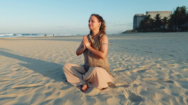 Young woman practicing mindfulness meditation on a tranquil beach, sitting in a yoga pose with closed eyes, hands in namaste mudra, finding inner peace and spiritual wellness at sunset
