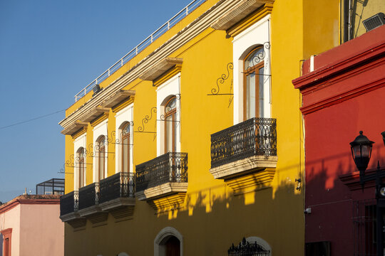 View of a vibrant yellow colonial building with black wrought-iron balconies and arched windows under a clear blue sky in Oaxaca, Oaxaca, Mexico.