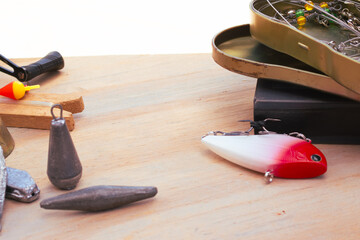 Fishing gear laid out on a wooden background: red-and-white lure, lead weights, bobber and open tackle box with hooks, swivels and pliers for an angling setup © Vero Dibe