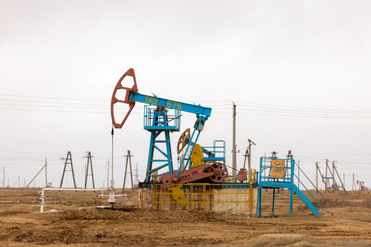 View of a blue pumpjack operating in an oil field with power lines and a barren landscape in Zhanaozen, Mangystau Region, Kazakhstan.