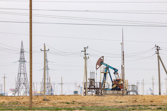 View of an oil pumpjack operating in an oil field with power lines and electrical infrastructure in the desert landscape of Zhanaozen, Mangystau Region, Kazakhstan.