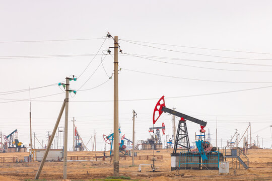 View of oil pumpjacks operating in an oil field with power lines and industrial equipment under a hazy sky in Zhanaozen, Mangystau Region, Kazakhstan.