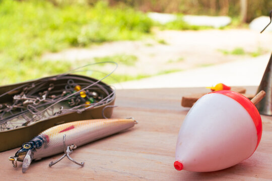 Fishing gear spread out on a wooden surface, including a colorful lure, a sinker, a float and a box of hooks, preparing for a relaxing day of fishing. High quality photo.