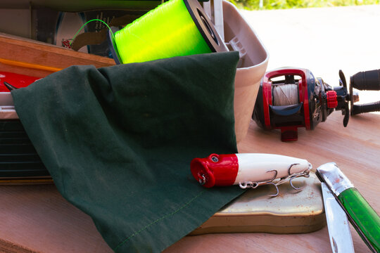 Fishing equipment on a wooden surface. Including a fishing reel with line. A bright green spool of fishing line. A red and white fishing lure. And a pocket knife