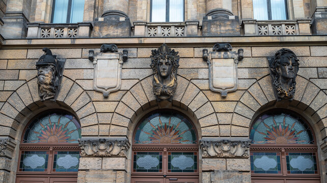 Ornate historic building facade in Dresden, Germany. Detailed stone mascaron sculptures and stained glass windows above arches. Neo-Renaissance architecture heritage