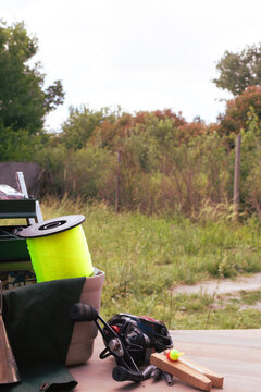 Fishing tackle arranged on a wooden surface with a bright yellow line spool, black baitcasting reel, bobbers and weights against a soft green outdoor background, ready for angling