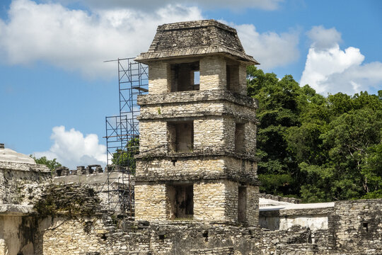 View of the ancient stone tower at the Palenque archaeological site, featuring weathered masonry and restoration scaffolding against lush jungle and blue sky in Palenque, Chiapas, Mexico.