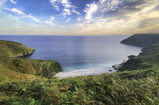 View of Lantic Bay with turquoise waters, sandy beach, and lush green cliffs under a soft sky at golden hour in Fowey, England, United Kingdom.
