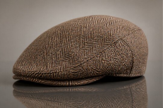 Brown tweed flat cap resting on reflective studio surface