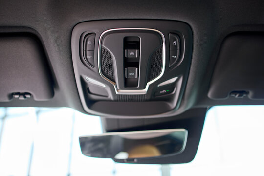 Illuminated vehicle overhead console with map lights, control buttons, speaker grille, textured ceiling panel, and soft gray trim inside modern car interior, with overhead, console, map, light detail
