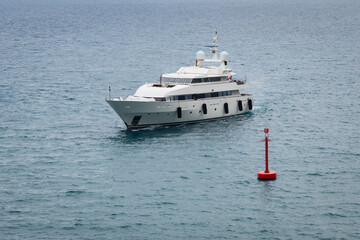 Luxury white motor yacht cruising on the blue waters of the Mediterranean Sea near a red navigational buoy off the coast of Nice, France. © Dmitri
