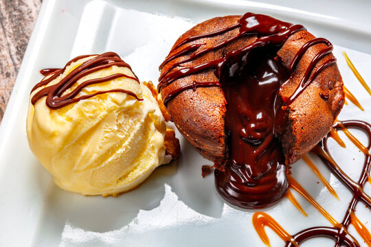 Decadent chocolate lava cake with a gooey molten center, served with vanilla ice cream and syrup.