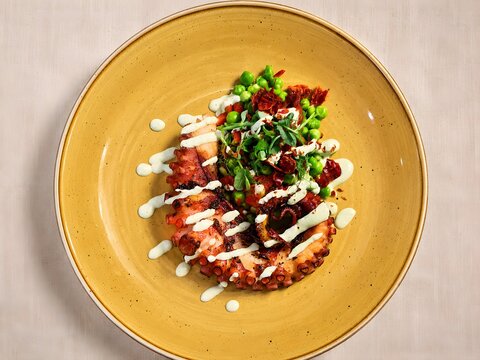 Grilled Octopus with Green Peas, Fresh Herbs and Creamy Sauce on Ceramic Plate