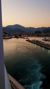 Aerial view from sea of Bodrum marina with yachts moored near white coastal town and mountains under warm sunset light, Bodrum, Turkey. Handheld, Vertical video