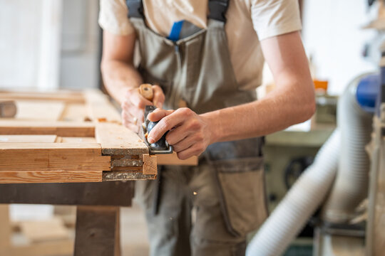 Craftsman flattering surface of antique wooden door with hand plane tool at workbench in studio, handicraftsman smoothing and shaping surface of furniture with plane instrument in restoration workshop