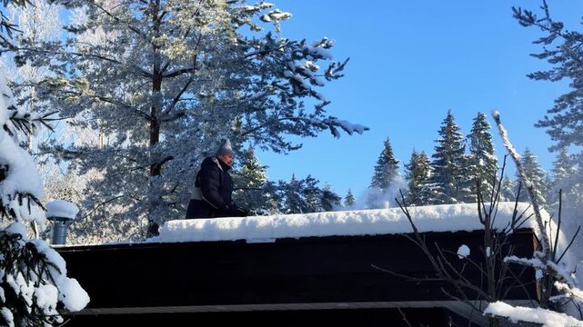Snow Removal Process. Man uses handheld battery snow blower to clear snow from roof of modern glass gazebo in pine forest bright winter sunlight, shot handheld, 4k footage