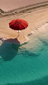 Vertical video: Pulling back drone camera revealing red umbrella, shadow on sand, to show blue sea