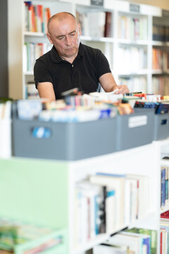 Adult man stands in bookstore, carefully browsing shelves and selecting book of interest