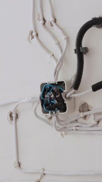 Close-up of organized white electrical cables and junction box on a light wall during home renovation. Wiring installation and electrical work footage