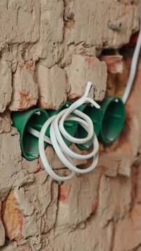 Close-up of a white electric wire coiled near green electrical outlet boxes on a rough brick wall during renovation. Construction and wiring concept