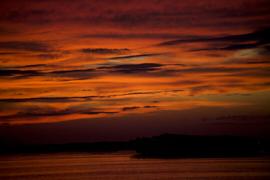 Intense fiery orange sunset sky with dramatic clouds reflected on calm water at dusk