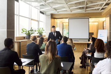 Obraz premium Businesspeople team at training seminar with coach. In a modern office, the coach leads a presentation by a screen as a group attends the meeting. Concept image of corporate training.