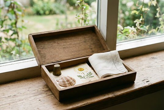 Small reminiscence memory box with simple treasured keepsakes resting on a bright windowsill. Gentle daylight, calm, uncluttered, nostalgia, remembering the past with copy space.
