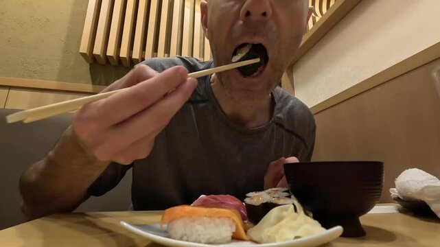 A person picks up a piece of salmon nigiri sushi with chopsticks from an assorted platter at a Japanese restaurant in Japan, with maki rolls, pickled ginger and a bowl of miso soup on the table &mdash; a ge