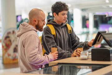 Fototapeta premium Man and teenage boy at a cafe counter with a touchscreen