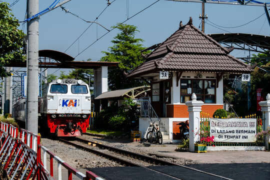 Yogyakarta, Indonesia - August 30, 2026: A KAI long-distance passenger train led by a CC206 diesel-electric locomotive passes a traditional Joglo-style crossing guard post near Yogyakarta Tugu Railway