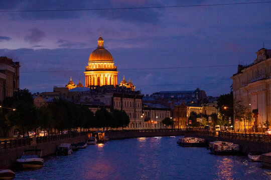 Historic city river canal with cruise boat and illuminated cathedral dome at twilight blue hour.
