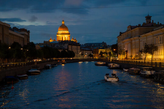 Historic city river canal with cruise boat and illuminated cathedral dome at twilight blue hour.
