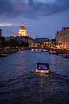 Historic city river canal with cruise boat and illuminated cathedral dome at twilight blue hour.
