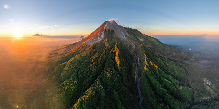 Aerial view of Mount Merapi at sunset with lush green slopes and deep volcanic ravines in Cangkringan, Special Region of Yogyakarta, Indonesia.