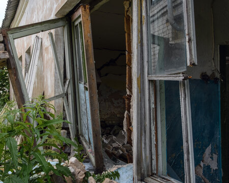 Close-up of a destroyed wooden window frame and collapsed wall with debris in an abandoned house.