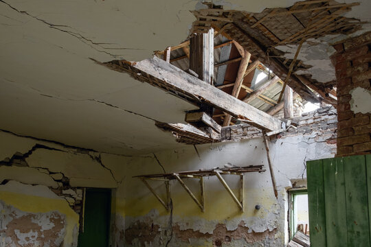 Interior view of a collapsed ceiling exposing wooden roof beams and rafters in an abandoned ruined building.