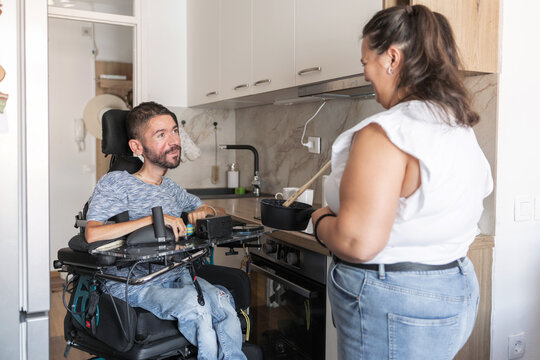 Personal assistant and wheelchair user enjoying cooking together and tasting a homemade meal during their daily home routine.