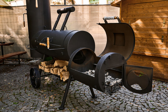 Black metal smoker grill with wood storage on cobblestone patio