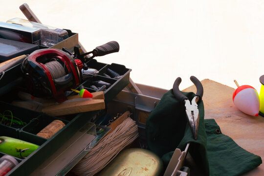 Fishing equipment and accessories are packed into a tackle box, showcasing a collection of lures, bobbers, a reel, line, and pliers, ready for an outdoor fishing adventure