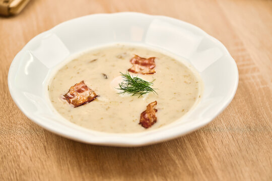 Creamy soup with bacon pieces and fresh dill in a white bowl